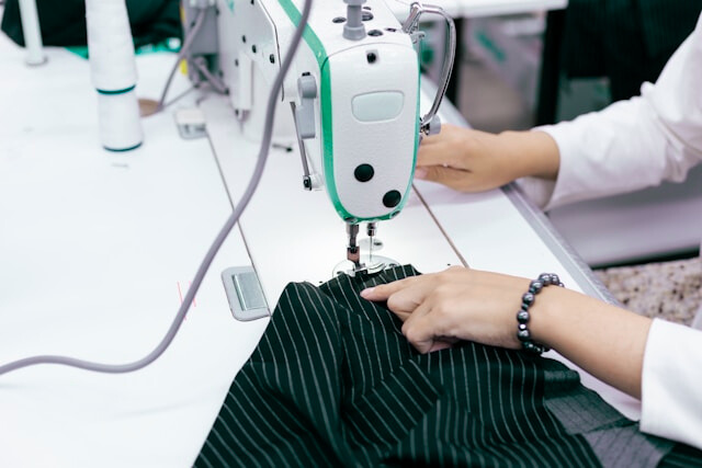 Dettaglio di sarta al lavoro su macchina da cucire industriale per la confezione di abbigliamento Made in Italy.